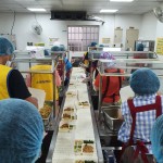 新業(yè)同仁與志工們繫上圍裙、套上防塵帽，戴上口罩，手捧一份份飯包各司其職，為的是準(zhǔn)時(shí)將熱騰騰的飯包送到長(zhǎng)輩手中。