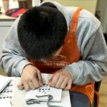 小羊苗朋友將臉湊近提袋上，仔細將貼紙慢慢地貼上，盡可能確保貼紙有貼正不歪斜。從肢體動作，可以曉得小羊們做每件事比別人費力，但不減心意。